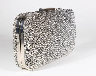 May include: A silver clutch purse covered in small, round beads. The purse has a silver clasp and a rectangular shape.
