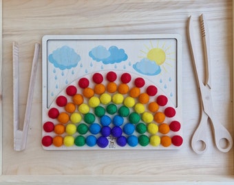 May include: A wooden rainbow sorting tray with colourful felt balls and a pair of wooden tweezers. The tray has a picture of clouds and rain on it.