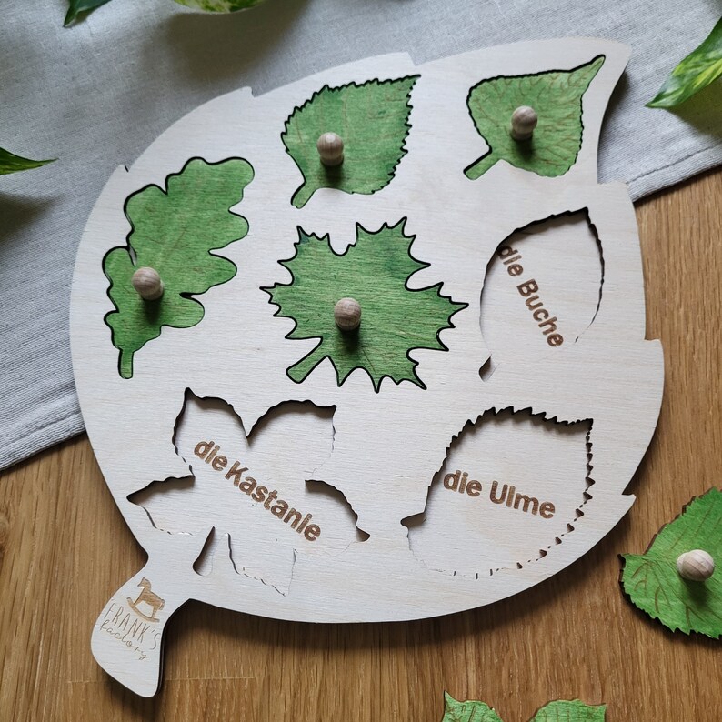 May include: Wooden leaf-shaped puzzle with six different leaf shapes and names in German. The names are "die Buche", "die Ulme", "die Kastanie", and three unnamed leaves.