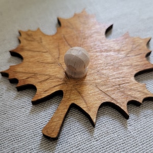 May include: A wooden maple leaf with a natural wood finish and a small wooden knob in the center.