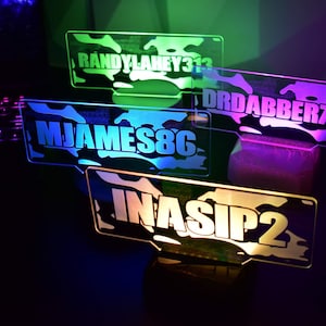 May include: Four personalized LED light signs with camouflage patterns and white text. The signs read "RANDYLAHEY313", "DRDABBER710", "MJAMES8G", and "INASIP2".