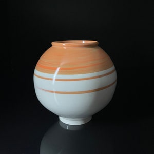 May include: A white ceramic vase with a rounded shape and a wide opening. The vase is decorated with horizontal stripes of orange and white.