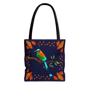 May include: A tote bag with a vibrant bird illustration. The bird, perched on a branch, features colorful plumage in shades of green, orange, and blue. The background is a deep navy blue, adorned with orange butterfly accents. The bag has black handles.