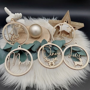 May include: Five wooden Christmas ornaments with names written on them. The ornaments are decorated with reindeer and snowflakes. The names on the ornaments are "Kim", "Diana", "Lucy", "Mama", and "Lisa".