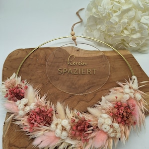 May include: A gold metal hoop with a dried flower wreath in shades of pink and white. The hoop has a clear acrylic sign with the text "herein spaziert" in gold lettering.