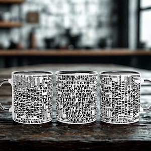 Puede incluir: Tres tazas de cerámica blanca con interiores y asas negras se exhiben sobre una superficie de madera. Cada taza está cubierta de texto negro relacionado con los tatuajes. El texto incluye frases como "artista del tatuaje" y "máquinas y magia".
