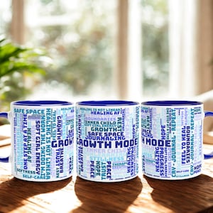 May include: Three white ceramic mugs with blue handles and rims, each featuring a word cloud design in shades of blue and white. The mugs are on a wooden surface, with a plant in the background. The word cloud includes words like "Growth", "Healing", and "Safe Space".