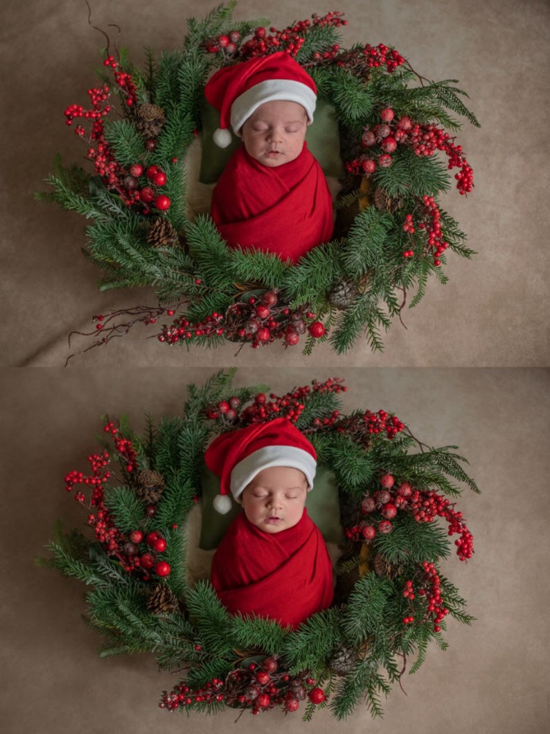 Op de afbeelding: Een pasgeboren baby die een rode kerstmanmuts en een rode swaddle draagt, slaapt in een groene kerstkrans versierd met rode bessen.