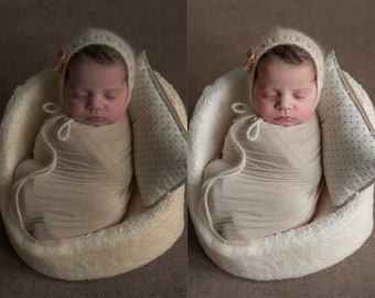 Op de afbeelding: Een pasgeboren baby slaapt in een wit, pluche, ovaalvormig bed. De baby draagt ​​een witte gebreide muts met een klein strikje en is gewikkeld in een wit dekentje. De baby ligt op een wit kussen met kleine bruine stippen.