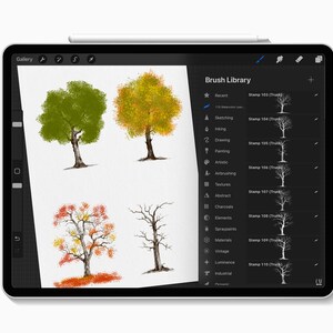 May include: Digital art on a tablet featuring four tree illustrations in various stages of the seasons. The tablet's screen displays a "Brush Library" with different artistic tools. A stylus rests on the top edge.