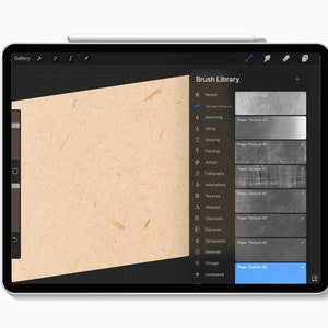 Puede incluir: Una tableta digital que muestra la interfaz "Brush Library" de una aplicaci&oacute;n de dibujo. La pantalla muestra varias texturas de papel, incluyendo "Paper Texture 45". Un l&aacute;piz &oacute;ptico descansa en la parte superior. Una textura de papel marr&oacute;n se muestra a la izquierda.