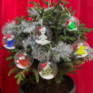 May include: A Christmas tree decorated with six clear glass baubles. Each bauble contains a small, colourful, Lego-style figure wearing a Santa hat. The baubles are surrounded by silver tinsel.