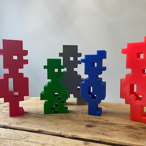 Peut inclure: Cinq figurines d'art pixel, chacune représentant un personnage différent. Les figurines sont en plastique et peintes dans différentes couleurs, notamment le rouge, le vert, le bleu et le gris.