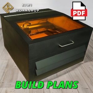May include: A black laser cutter with a clear lid and an orange light inside. The laser cutter is sitting on a wooden floor. The text "BUILD PLANS" is written in green letters below the laser cutter. The text "PDF" is written in white letters on a white document icon.