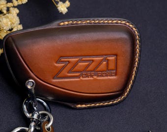 May include: Brown leather key fob cover with the embossed text "Z71 OFF ROAD". The key fob cover has a stitched border and a metal key ring attached. The leather is a rich, dark brown color.