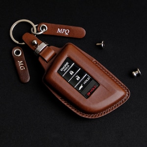 May include: Brown leather key fob with a silver key ring and two leather tags that say "MPQ" and "MG". The key fob has a black plastic key with buttons that say "Engine Hold", "Hold", and "Hold".