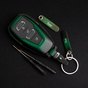 May include: A green leather key fob with a silver key chain and two small screwdrivers. The key fob has the names "Toro" and "Sue" engraved on it.