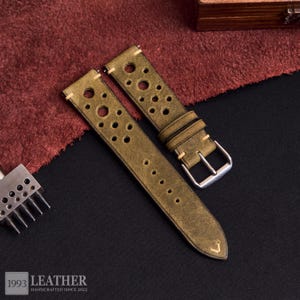 Puede incluir: Correas de reloj de cuero verde oliva con m&uacute;ltiples perforaciones circulares. Las correas tienen un aspecto vintage, con costuras visibles y una hebilla plateada. El texto "1993 LEATHER HANDCRAFTED SINCE 2022" es visible en la parte inferior.