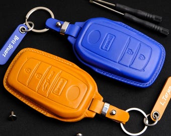 May include: Two leather key covers for car keys. One is orange and the other is blue. Both have a key ring attached.