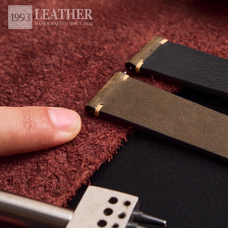 May include: Close-up of two leather watch straps, one black and one olive green, with gold stitching. The straps are handcrafted and the image includes the text "1993 LEATHER HANDCRAFTED SINCE 2022".