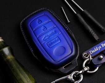 May include: A blue leather key fob with a black stitching detail. The key fob has a car key shape and a metal hook for attaching to a keychain.
