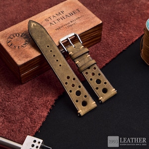 Puede incluir: Correa de reloj de cuero verde oliva con agujeros perforados y costuras color crema. La correa tiene una hebilla plateada y se muestra con una caja de madera de sellos de alfabeto. El texto "1993 LEATHER HANDCRAFTED SINCE 2022" es visible.