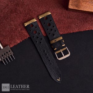 Puede incluir: Correas de reloj de cuero negro con herrajes de metal color lat&oacute;n. Las correas tienen un dise&ntilde;o perforado y una hebilla plateada. La imagen tambi&eacute;n muestra una herramienta de artesan&iacute;a en cuero y el texto "1993 LEATHER HANDCRAFTED SINCE 2022".