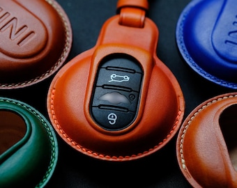 May include: A set of five leather key covers for a car key fob. The key covers are in different colors, including brown, blue, green, and orange. The key covers are stitched with a contrasting thread. The key covers are designed to protect the car key fob from scratches and wear.