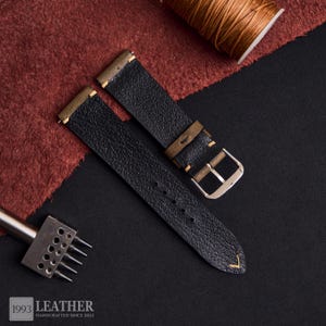 May include: Black leather watch straps with tan accents and a silver buckle. The straps are textured and feature yellow stitching. The image also includes a spool of thread, a leather punch tool, and the text "1993 LEATHER HANDCRAFTED SINCE 2022."