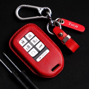 May include: Red leather key fob with a silver key chain and a silver tag that says "Tonja".