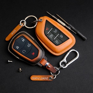 Puede incluir: Dos llaveros de cuero marrón con anillas metálicas y un mosquetón plateado. Un llavero tiene el texto "DON'T PANIC" y el otro el texto "CITY".