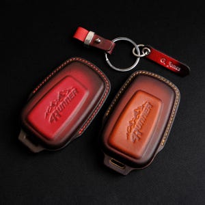 May include: Two leather keychains with a red and brown color gradient. Both keychains have the word "4RUNNER" embossed on them. The keychain on the left has a red gradient and the keychain on the right has a brown gradient. The keychains are attached to a silver key ring. The keychain on the right has a small leather tag with the name "G. Jones" embossed on it.
