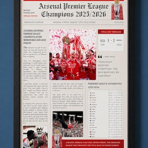 May include: A framed commemorative poster titled Arsenal Premier League Champions 2025/2026, featuring red and white text, a photograph of players celebrating with a trophy, a match score box, a league table, and descriptive articles on a cream background.