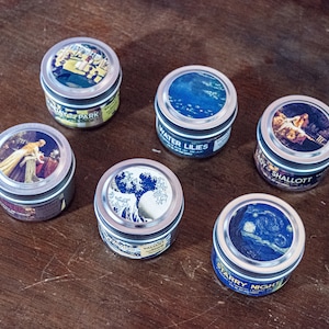 Puede incluir: Seis latas redondas de metal con diferentes imágenes en las tapas. Las latas están dispuestas en círculo sobre una superficie de madera. Las imágenes incluyen una escena de un parque, nenúfares, una mujer en un bote, un árbol, una noche estrellada y una mujer con un vestido rojo.