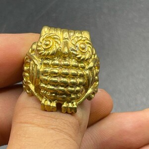 May include: A gold owl ring with detailed features. The owl's eyes are round and have a raised design. The owl's body is covered in small, raised dots.