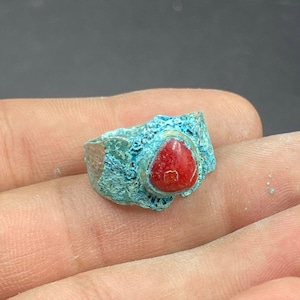 Könnte beinhalten: Ein silberner Ring mit einem roten Korallen-Stein, der in einer türkisfarbenen Metallfassung sitzt.