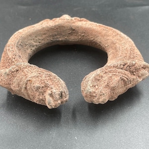 May include: A large, ornate, brown metal bracelet with intricate details. The bracelet is made of a thick, heavy metal and has a rough, textured surface.