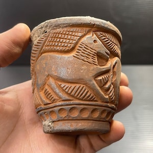 Puede incluir: Una taza de terracota con un diseño tallado de un caballo. La taza tiene un esmalte marrón y una banda decorativa alrededor del borde.