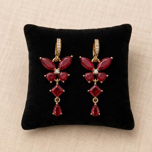 May include: A pair of gold-tone drop earrings featuring a butterfly motif crafted from marquise and heart-shaped red stones. Each earring includes a central clear stone, a square-cut red stone, and a teardrop-shaped red stone, with pavé-set clear stones.