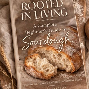 May include: A cookbook titled "ROOTED IN LIVING" with the subtitle "A Complete Beginner's Guide to Sourdough" is displayed open, revealing a sliced loaf of bread. The book cover is light brown with white text. The image includes wheat stalks and a jar.
