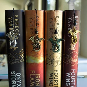 May include: Four books with dragon-themed bookmarks. The book spines are in shades of black, orange, and burgundy, with titles like "Onyx Storm," "Iron Flame," and "Fourth Wing." Each bookmark features a metal dragon charm.