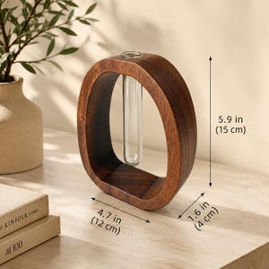 Puede incluir: Un jarr&oacute;n de madera de color marr&oacute;n oscuro con forma ovalada, con un tubo de vidrio para una sola flor. El jarr&oacute;n mide 15 cm de alto, 12 cm de ancho y 4 cm de grosor. El dise&ntilde;o incluye un tubo de vidrio transparente.