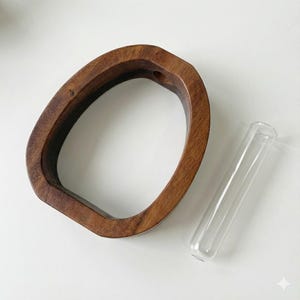 Puede incluir: Un jarr&oacute;n de madera de forma ovalada y color marr&oacute;n oscuro. Un tubo de vidrio transparente est&aacute; colocado junto al jarr&oacute;n. El jarr&oacute;n tiene un agujero en la parte superior. Los objetos est&aacute;n sobre una superficie blanca.