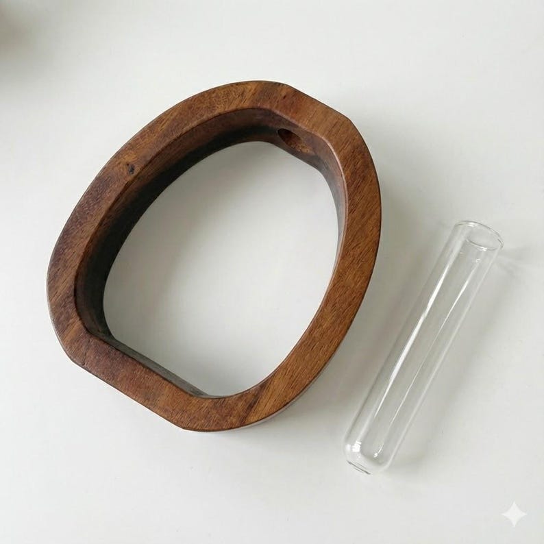 Puede incluir: Un jarr&oacute;n de madera de forma ovalada y color marr&oacute;n oscuro. Un tubo de vidrio transparente est&aacute; colocado junto al jarr&oacute;n. El jarr&oacute;n tiene un agujero en la parte superior. Los objetos est&aacute;n sobre una superficie blanca.