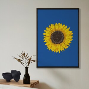 May include: A framed print of a yellow sunflower on a blue background. The sunflower is drawn in a simple, stylized way.