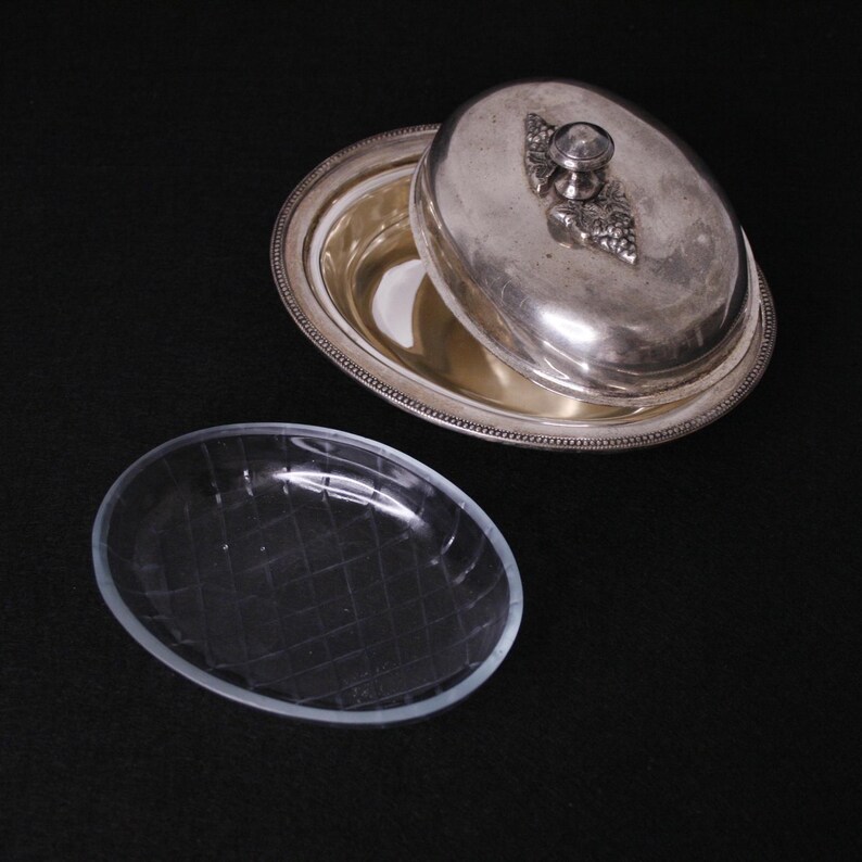 May include: A silver butter dish with a lid and a glass insert. The lid has a grape design on the knob.