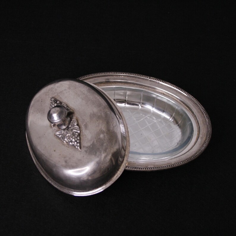 May include: Silver oval butter dish with a glass insert and a lid with a grape design.