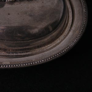 May include: Close-up of a silver butter dish with a beaded edge. The lid is slightly ajar, revealing the smooth, silver interior.