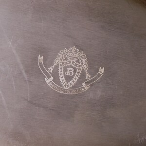 May include: A silver serving tray with an engraved crest featuring a shield with the letter "B" inside, surrounded by a wreath and a banner that reads "Sheffield Collection".