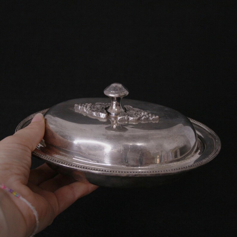 May include: A silver oval serving dish with a lid. The lid has a decorative knob and a floral design.